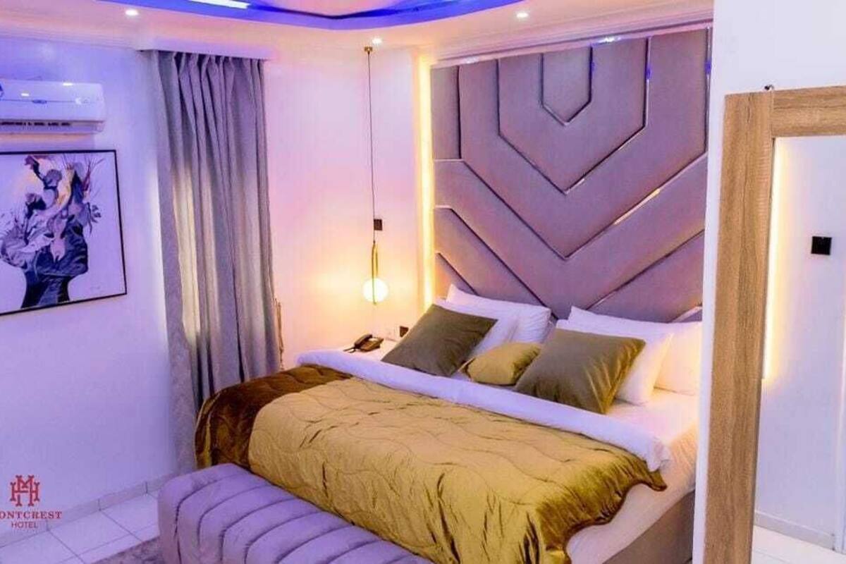Une chambre moderne avec un grand lit, une tête de lit ornée de motifs géométriques, une table de chevet et un climatiseur fixé au mur.