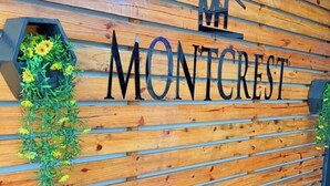 A wooden wall with the name "MONTCREST" in large letters. There are two planters with green plants and yellow flowers. - Montcrest Hotel & Lounge (Port Harcourt)
