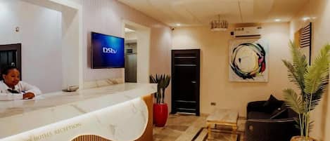 A hotel reception area with a marble counter, a television mounted on the wall, and a reception desk.