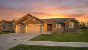 A residential house with a garage, a driveway, and a well-maintained lawn. - Modern Home with 3-Car Garage & Large Yard (Idaho Falls)