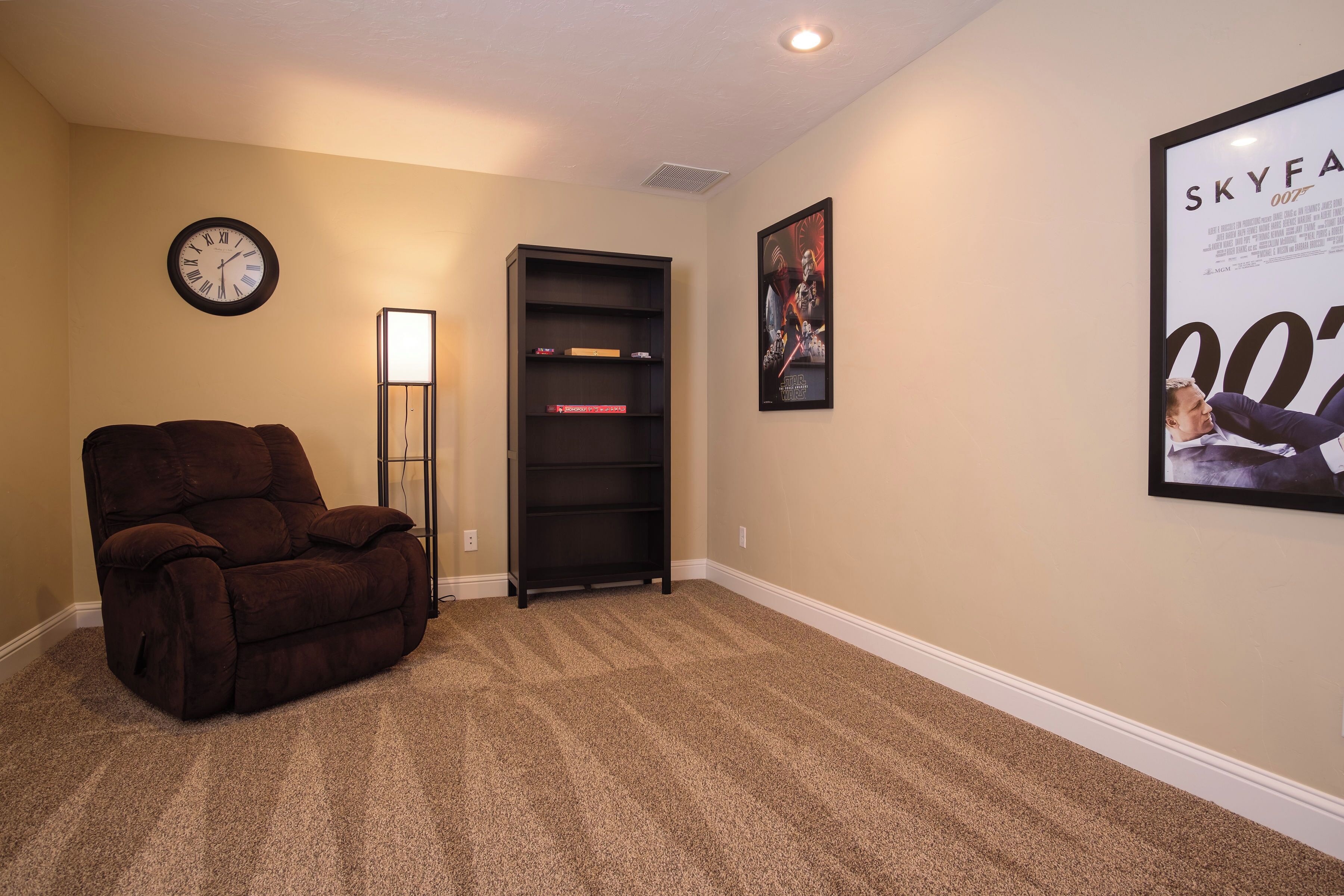 A living room with a recliner, a bookshelf, a clock, and a movie poster on the wall.