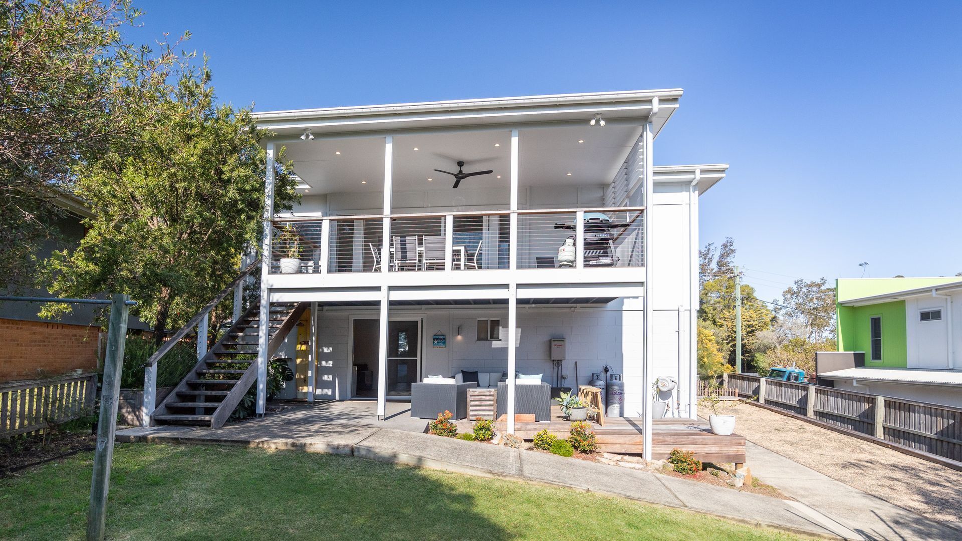 A two-story building with a balcony on the upper floor, a staircase leading to the entrance, and a small outdoor seating area.