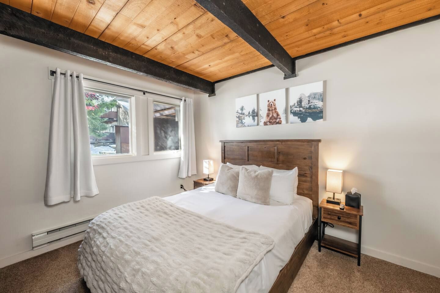 A bedroom with a wooden ceiling, a bed with white bedding, two bedside tables with lamps, and a window with curtains.