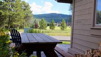 A wooden picnic table and chairs outside a building with a view of a forest and mountains.