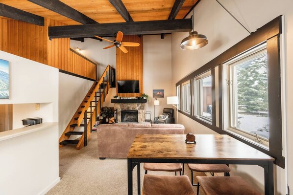 Un interior moderno con una escalera de madera, una chimenea, una mesa de comedor con sillas y un ventanal con vistas.