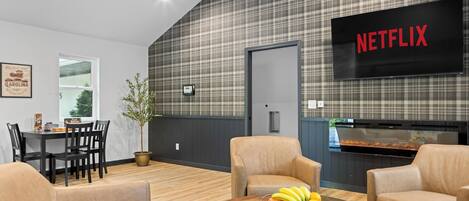 A modern living room with a dining area, a television displaying 'NETFLIX,' and a kitchen area.