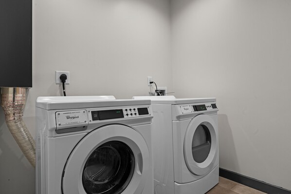 Two front-loading Whirlpool washers in a laundry room with a white wall and a black baseboard. - Lodge at Mount Mitchell (Burnsville)