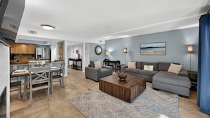 Uma sala de estar moderna com um sofá cinza, uma mesa de centro de madeira e uma área de jantar com mesa e cadeiras.