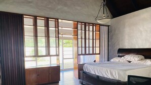 Een slaapkamer met een bed, een stoel, een kast en grote ramen.