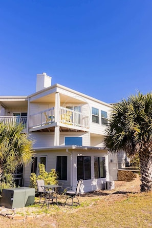A two-story house with a balcony, a patio with chairs, and a small garden area. - Flagler Beach Townhome—Steps to Sand! (Flagler Beach)