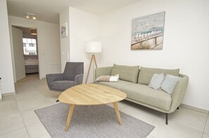 A living room with a sofa, a chair, a round wooden coffee table, a floor lamp, and a painting on the wall. - Beachfront vacation rental with a terrace, pool access, and a sauna - Rex Rugia - Rex (Göhren)