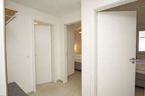 A hallway with white doors leading to a bedroom with a bed and a nightstand.