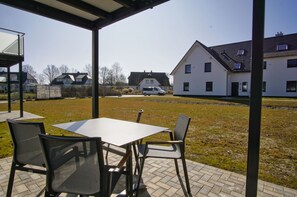 An outdoor patio with a table and chairs, a covered area, and a view of a residential area with houses and a van.