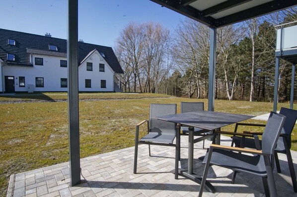 An outdoor patio with a table and chairs, a covered area, and a view of a white building and trees. - Beachfront vacation rental with a terrace, access to the pool and sauna - Rex Rugia - Rex (Göhren)