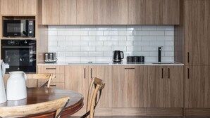 A modern kitchen with wooden cabinets, a white tiled backsplash, a built-in oven, a coffee maker, and a dining area with a wooden table and chairs.
