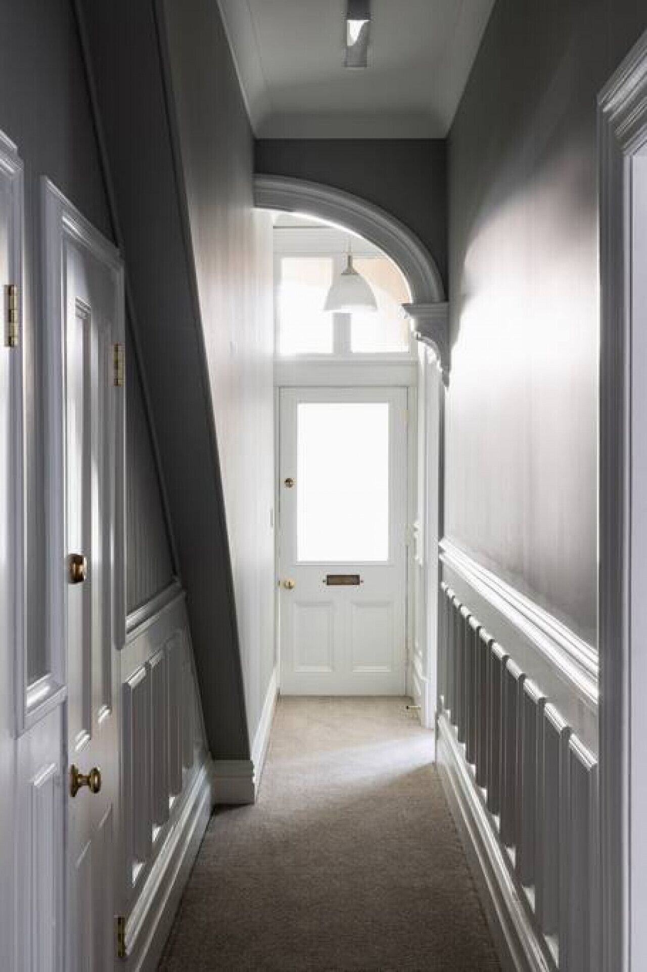 A narrow hallway with white doors and a white-framed window at the end.