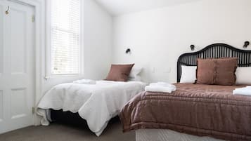 A bedroom with two single beds, white and brown bedding, a window with blinds, and a white door.