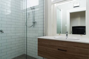 A bathroom with a glass shower enclosure, a sink with a mirror, and a wooden vanity. - The Octagon House (Dunedin)