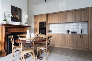 A modern kitchen with wooden cabinets, a white tiled backsplash, a dining table with chairs, and a fireplace with decorative items. - The Octagon House (Dunedin)