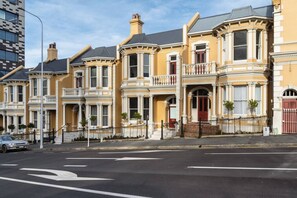 A row of Victorian-style townhouses with bay windows, a gated driveway, and a street view. - The Octagon House (Dunedin)