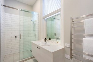 Une salle de bain moderne avec une douche à parois de verre, des murs recouverts de carreaux blancs, un lavabo blanc et un porte-serviettes.