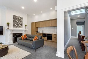 Un salon moderne avec un canapé gris, une cheminée et une cuisine dotée de meubles en bois et de carreaux blancs.