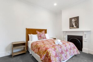 Ein Schlafzimmer mit Bett, Nachttisch, Kamin und einem gerahmten Bild an der Wand.
