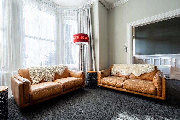 Ein Wohnzimmer mit zwei Ledersofas, einer roten Stehlampe und einem großen Fernseher an der Wand.