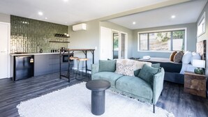 A modern living room with a sofa, a coffee table, and a kitchen area with a bar stool.