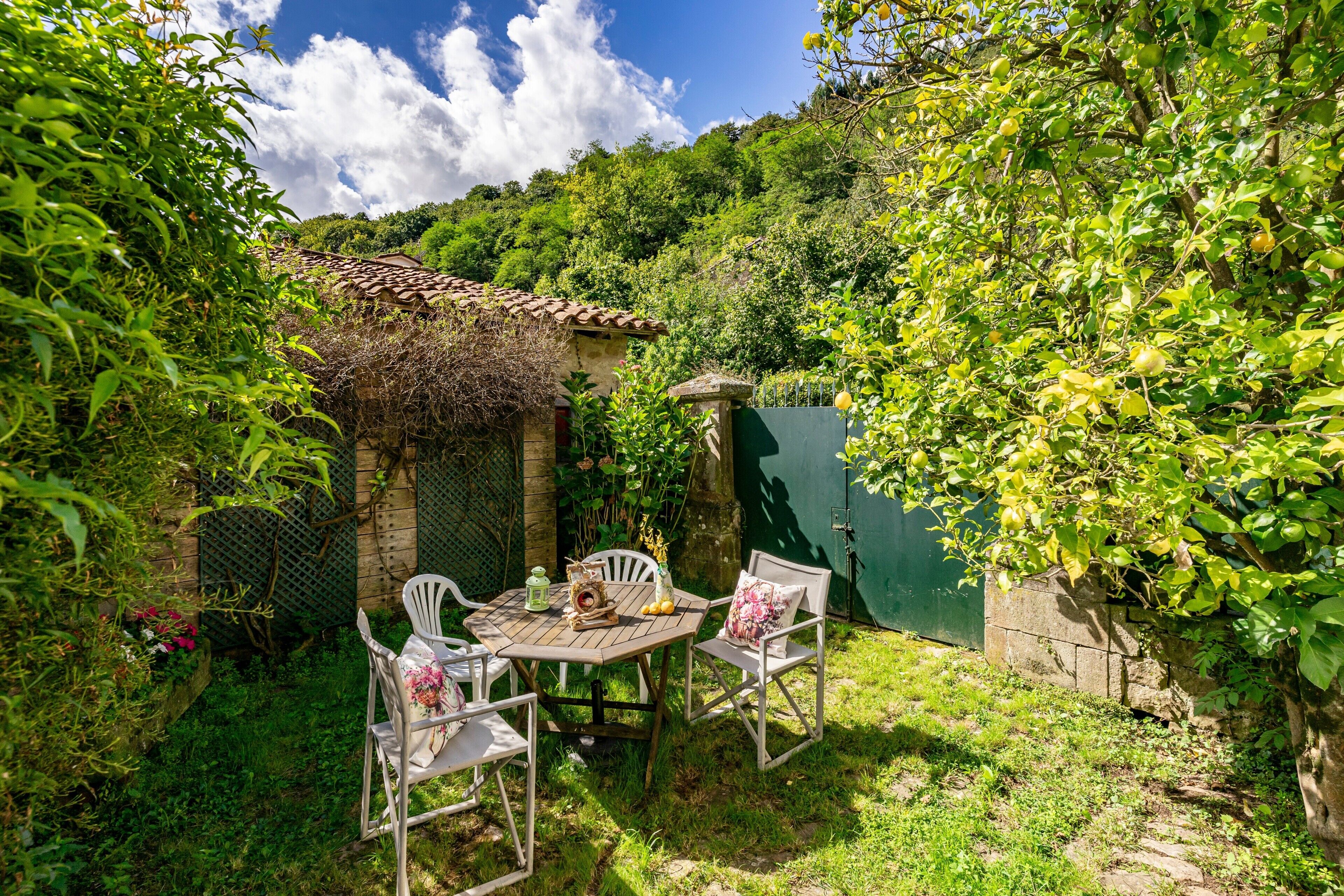A patio with a table and chairs, surrounded by greenery and a stone wall.