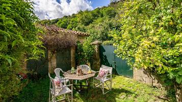 A patio with a table and chairs, surrounded by greenery and a stone wall.