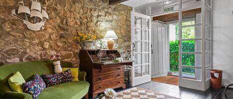 A room with a green sofa, a wooden dresser, a stone wall, a lamp, and a door labeled 'SALIDA'.