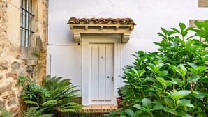 A white door with a tiled roof, a stone wall, and lush green plants.
