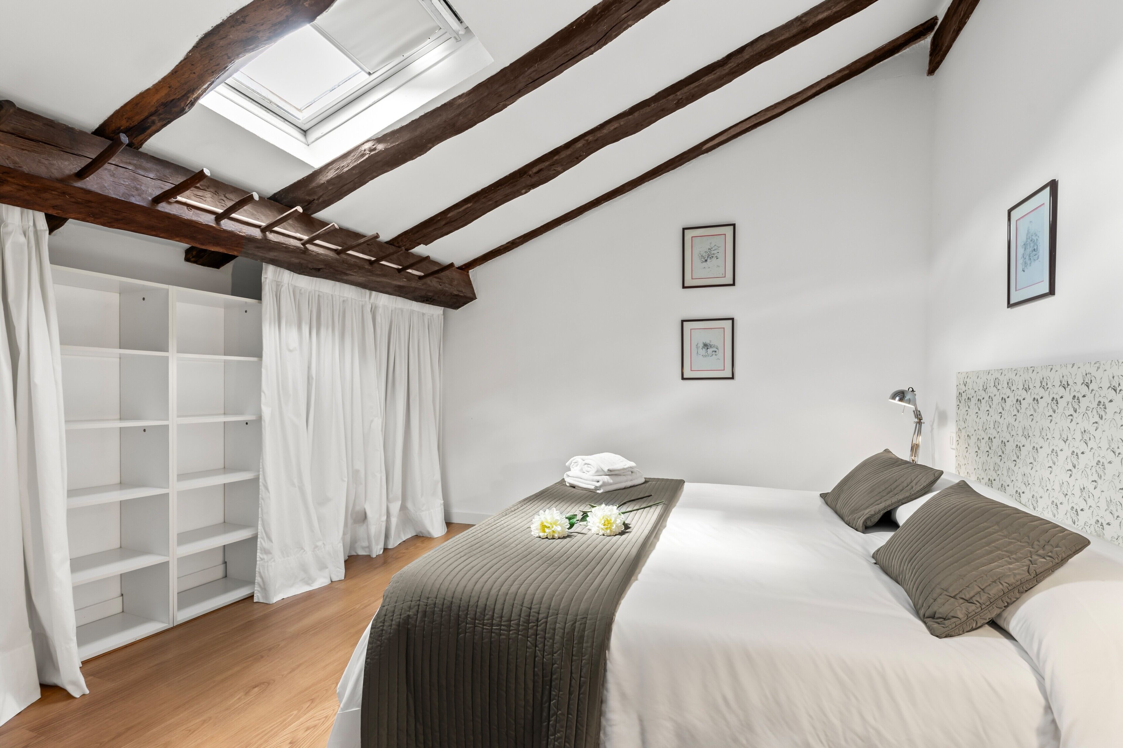 Een slaapkamer met dakraam, een kledingkast, een bed met kussens en een nachtkastje.