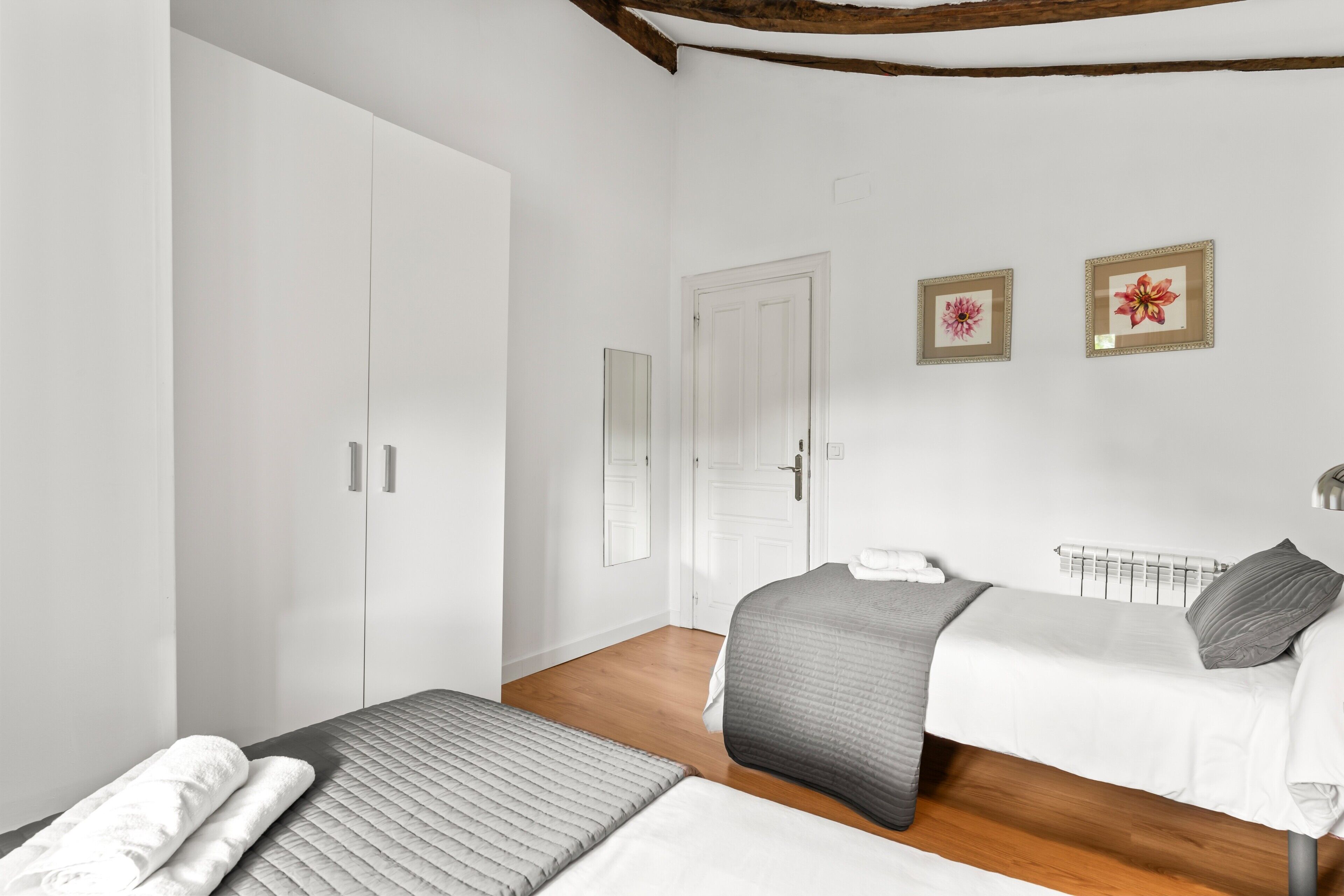 Una camera da letto con due letti, un armadio, un termosifone e due quadri appesi al muro.
