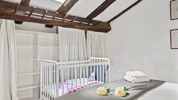 Un dormitorio con una cuna, una cama, un tragaluz y un armario blanco.