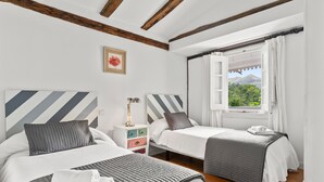 A bedroom with two beds, a nightstand, a lamp, and a window with curtains.