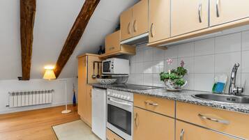 Una cocina con vigas de madera, armarios blancos, horno empotrado, microondas y un lavamanos.
