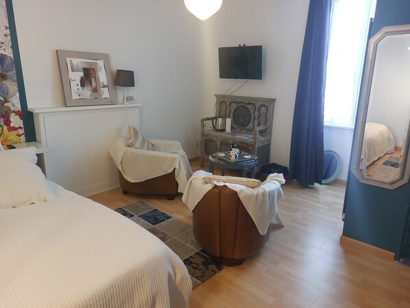 Habitación de hotel con cama, dos sillones, televisor, chimenea y ventana con cortinas.