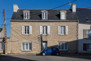A stone building with a car parked in front, a door, and a window with shutters.