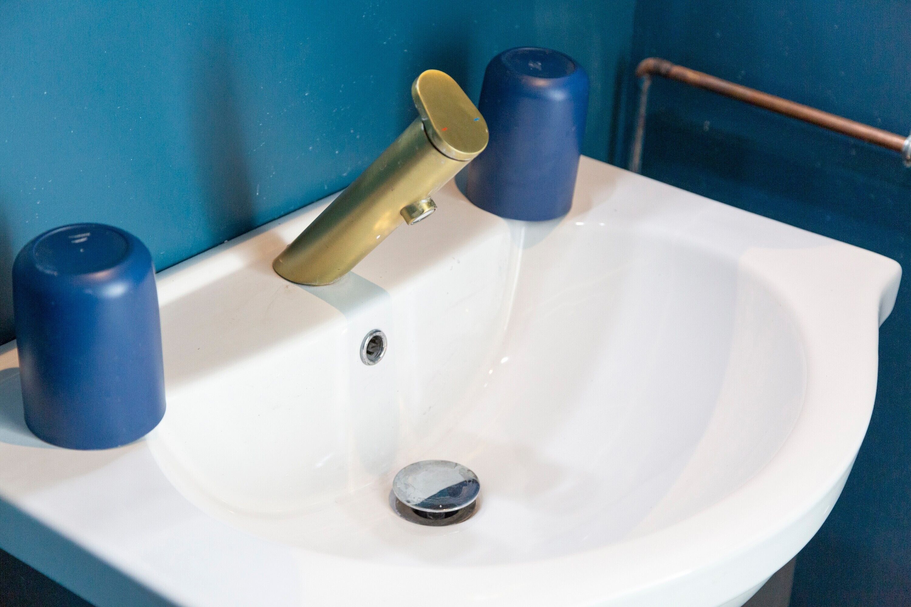 Ein weißes Waschbecken mit goldenem Wasserhahn, zwei blaue Seifenspender und einer Kupferleitung.