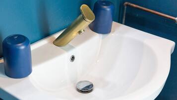 Ein weißes Waschbecken mit goldenem Wasserhahn, zwei blaue Seifenspender und einer Kupferleitung.