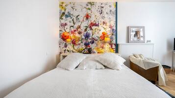 Une chambre à coucher avec un lit, des oreillers, une table de chevet, une lampe, un tableau encadré et une armoire en bois.