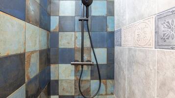 Ducha con cabezal de ducha y manguera de mano, frente a una pared con baldosas azules y color beige.
