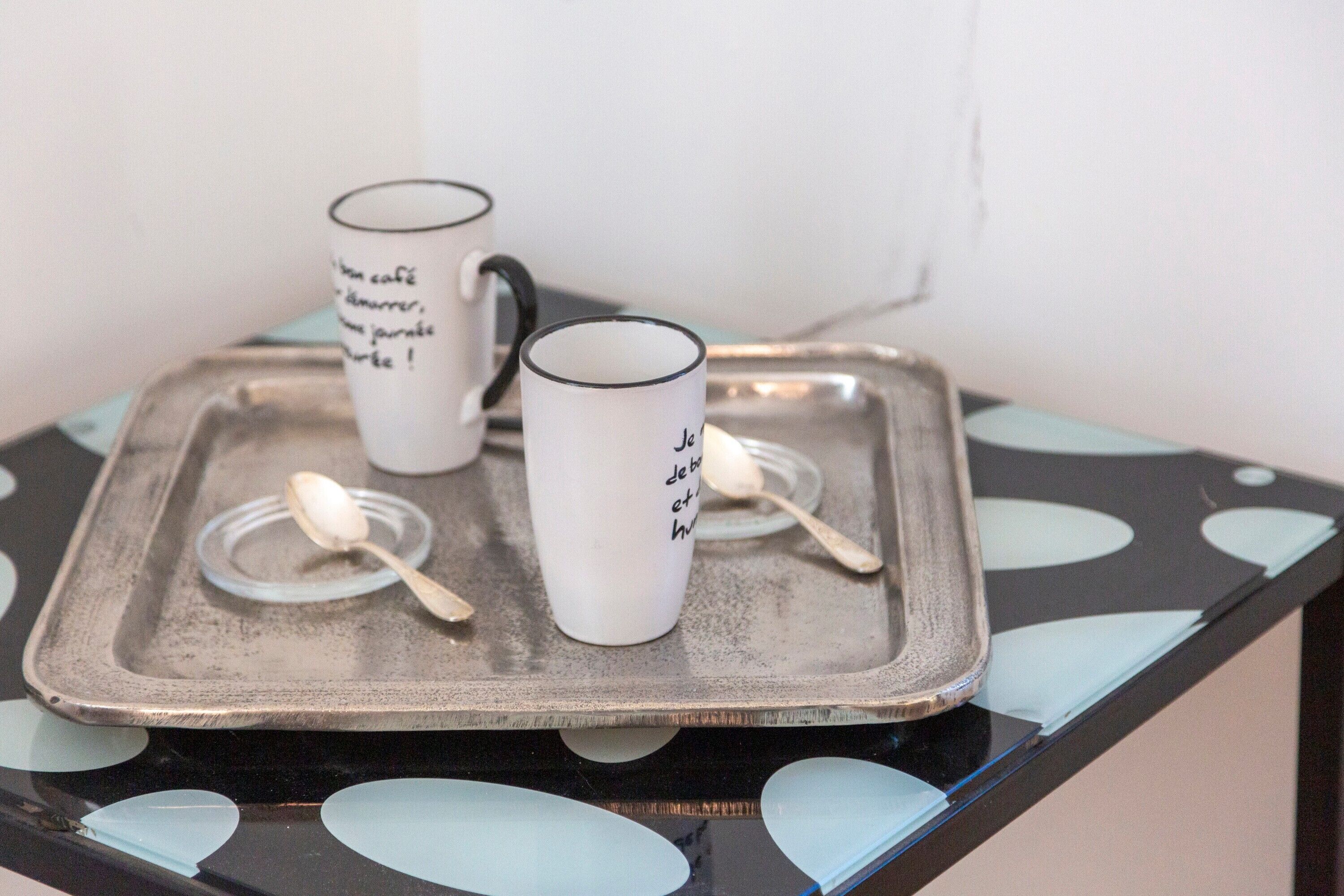 Een dienblad met twee witte mokken en twee lepels op een tafel met een zwart-wit patroon.