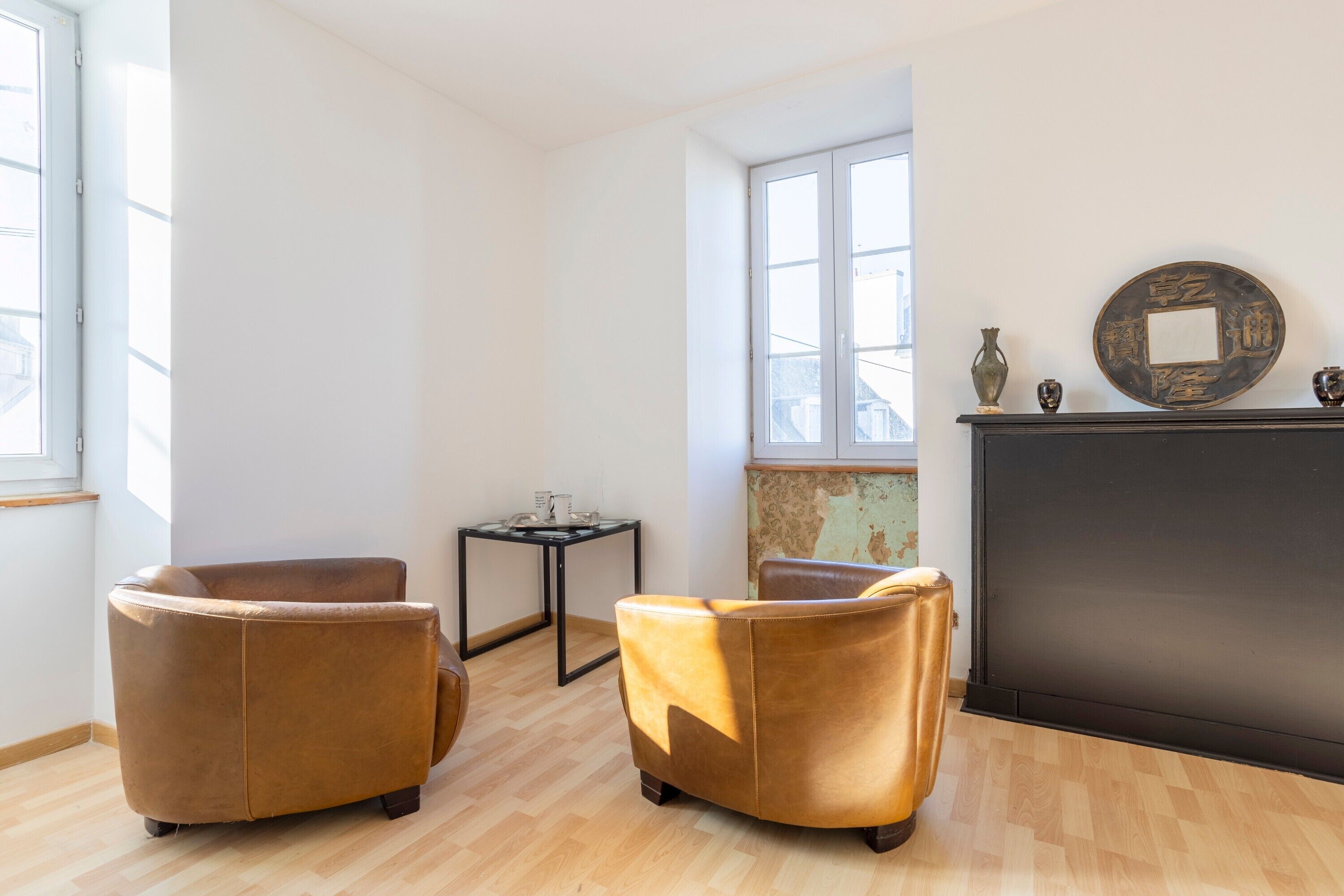 Une pièce comprenant deux fauteuils en cuir marron, une petite table, une cheminée et une grande fenêtre.
