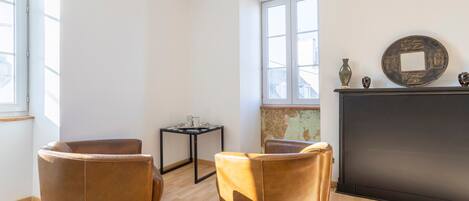 Une pièce comprenant deux fauteuils en cuir marron, une petite table, une cheminée et une grande fenêtre.