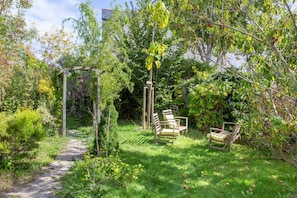 En have med en belægning af sten, en træpergola og to træstole.