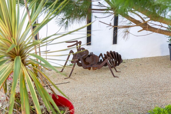 Une sculpture métallique représentant une araignée, dans un jardin, avec un bâtiment blanc en arrière-plan.