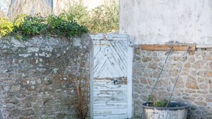 Un muro de piedra rústico, una puerta de madera blanca con un pestillo de metal y una planta en maceta.